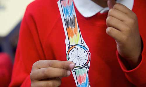 Primary school child showing off their handmade paper wristwatch.