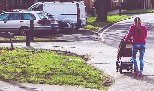 Young woman pushing pram through housing estate.