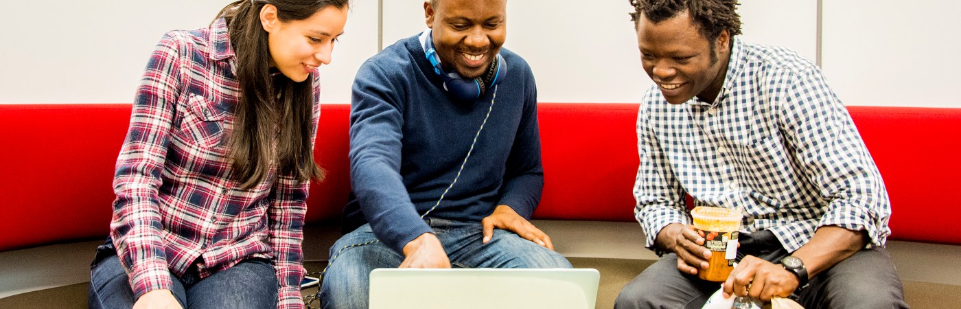 Three students sat around laptop laughing.