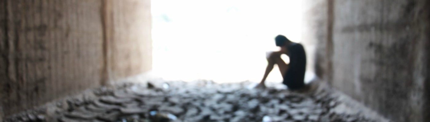 Backlight of an unhappy teenager sitting inside a dry soil tunnel, blurry background