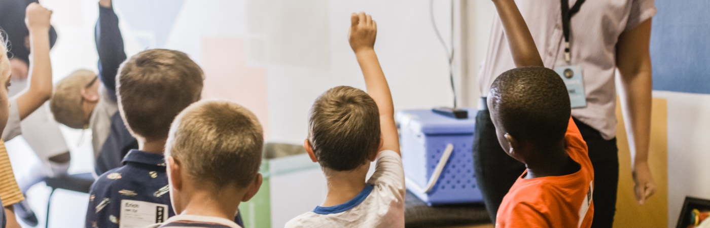 Children in classroom holding hands up.
