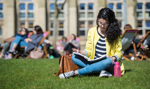 Student sat on the grass reading a book