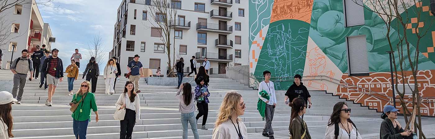 Students walk down wide steps in a modern area, beside a building with a large colourful mural.