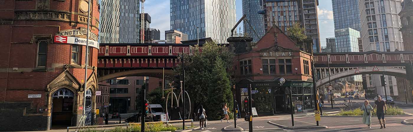 Historic red-brick buildings and railway bridge contrast with modern glass skyscrapers in Manchester
