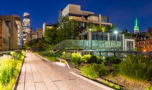 Panoramic view of the High Line promenade (Chelsea, Manhattan, New York City) at twilight with city lights and illuminated skyscrapers.