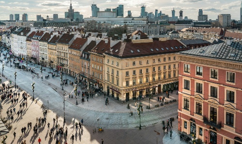 Busy pedestrian street lined with colourful historic buildings in Warsaw, with modern skyline in background.