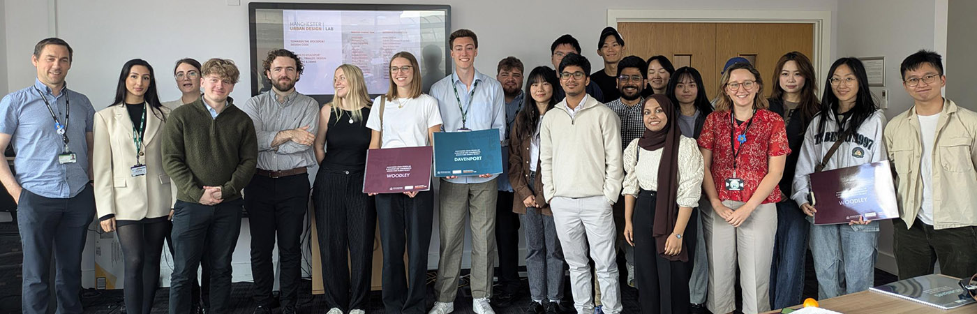 Group of students and faculty posing in a classroom setting, with some holding project folders.